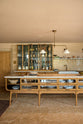 A warm and chic Haberdasher’s kitchen features an L-shaped sink and cooker run, countertop cupboards, a kitchen island, a Carrara and copper mix worktop, and a double-fluted marble sink. Adorned with artisan ceramics, a deVOL gaselier light, Heirloom wall lights, large vintage rugs, and engraved drinking glasses, this kitchen creates a warm and inviting Spanish-inspired space in Yorkshire.
