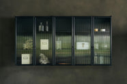 A bobbin black Haberdasher’s wall cupboard with reeded glass hangs on an olive limewash wall. Adorned with vintage white tin cases, empty glasses, and coral decorations, this space creates a lovely exhibitionist area that is both beautiful and practical.