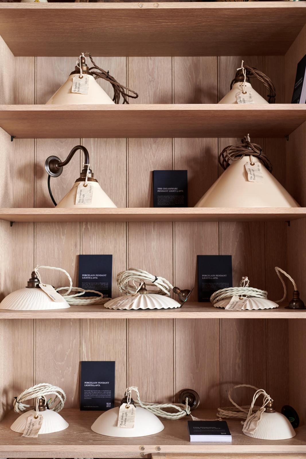 A closer look inside the glazed freestanding pantry cupboard reveals creamware and porcelain pendant lights as part of the handsome range of oak furniture and lighting from the deVOL Haberdasher’s collection. Adorned with fabric tags and deVOL postcards, this space creates a beautiful homage to the English gentlemen’s haberdashery inspiration in a bricked wall showroom.