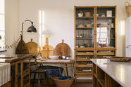 A warm and spacious Haberdasher’s kitchen features a sink run with a copper worktop, a small prep table with a Carrara marble countertop, and a freestanding pantry with glazed doors. Adorned with vintage furniture and items, artisan ceramics, wicker baskets, tea towels, large wooden tapas boards, and a delicate bird bunting in the corner of the window, this kitchen creates a contemporary yet nostalgic space.