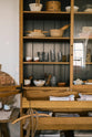 A closer look at a warm and spacious Haberdasher’s kitchen featuring a freestanding pantry with glazed doors. Adorned with vintage furniture and items, artisan ceramics, drinking glasses, tea towels, large wooden tapas boards, and wooden letterpress, this kitchen creates a contemporary yet nostalgic space.