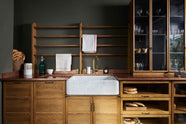 A closer look at a cosy and sophisticated Haberdasher’s kitchen features a sink run with a copper worktop, a single marble sink, glazed countertop cupboards, a freestanding pantry with glazed doors, and dark charcoal walls. Beautifully decorated with vintage furniture and items, wicker baskets, fresh bread, tea towels, and artisan ceramics, this kitchen creates a bright and warm space.