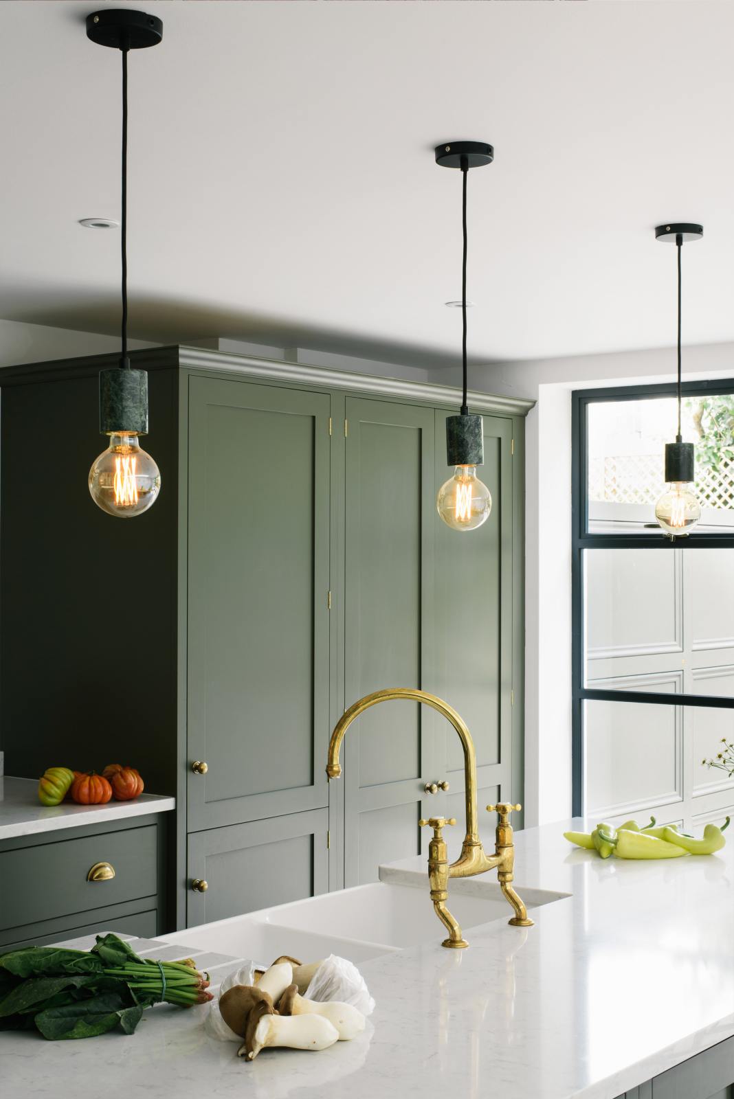 A close-up of the central island in a bright, sophisticated Bakehouse Green shaker kitchen, featuring a double Belfast sink with an aged brass Ionian tap and Silestone worktop, styled with Scandinavian furniture and a calming green palette.