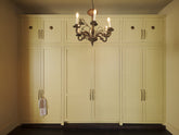 A simple corridor houses three sets of double cupboards; a pantry cupboard with a microwave, an integrated fridge/freezer cupboard, and a wine pantry cupboard with spice and bottle racks. Naturally decorated with a tea towel and an antique chandelier, creating a clean and organised storage space.