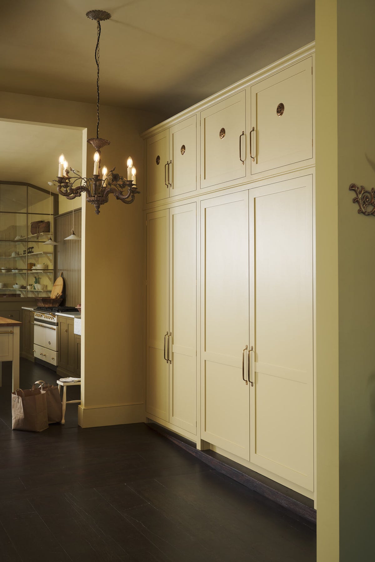 An oblique view of a simple corridor that houses three sets of double cupboards. Naturally decorated with brown grocery bags and an antique chandelier, creating a clean and organised storage space.