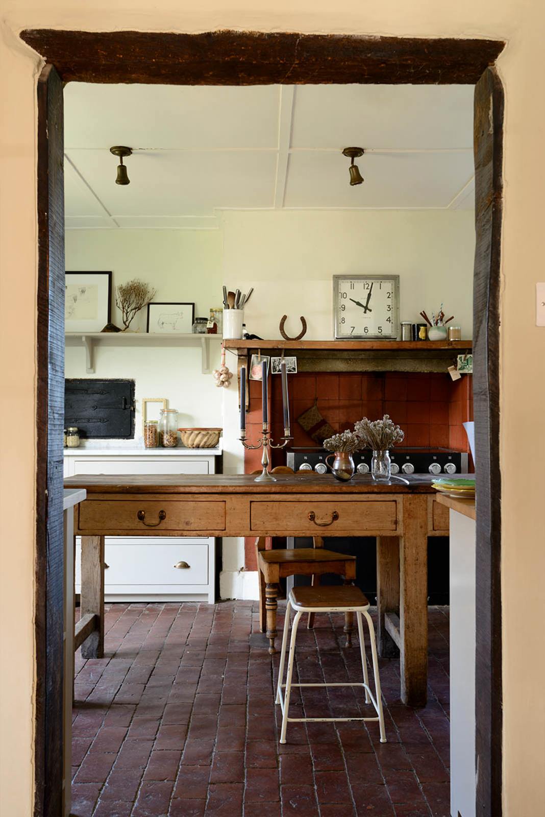 Pass the original farm’s solid oak archway is a small and quaint mushroom-coloured Shaker kitchen features a sink run made up of a mix of stave hardwood and Carrara marble worktops, a shelf, and a black stove nestled inside the original building’s chimney breast. Beautifully decorated with vintage furniture such as a large solid oak table, a silver scale, and assorted bric-a-brac, it creates a lovely social space full of character.