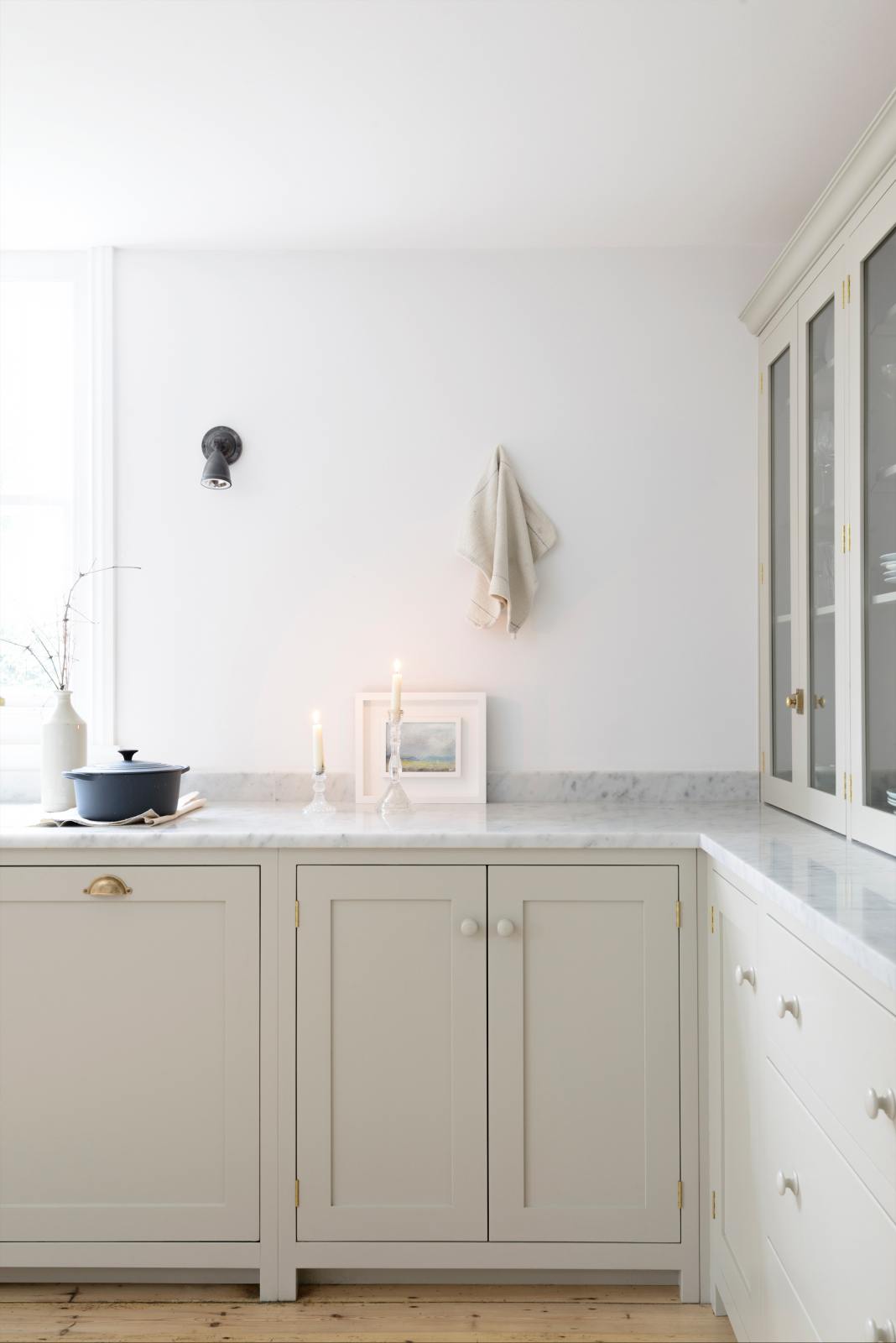 A quiet corner of a simple, mushroom-coloured shaker kitchen with a marble worktop and glazed cabinets peeking around the edge.