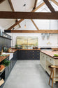 Nestled between an L-shaped cooker and sink run and a large white linen kitchen island topped with a stave hardwood worktop, the spacious pantry-blue Shaker kitchen has transformed a large, renovated cattle shed. Beautifully decorated with aged brass taps, Helen stools, luscious green vegetables, vintaged artisan ceramics, lilac tulips and abstract paintings.