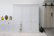 A spacious and artisan Shaker kitchen features an off-white L-shaped sink run with a Carrara marble worktop, a large pantry-blue kitchen island, and a bank of full-height cupboards. Cleverly decorated with vintage ceramics serving as artistic displays, it creates a simple yet intriguing kitchen space.