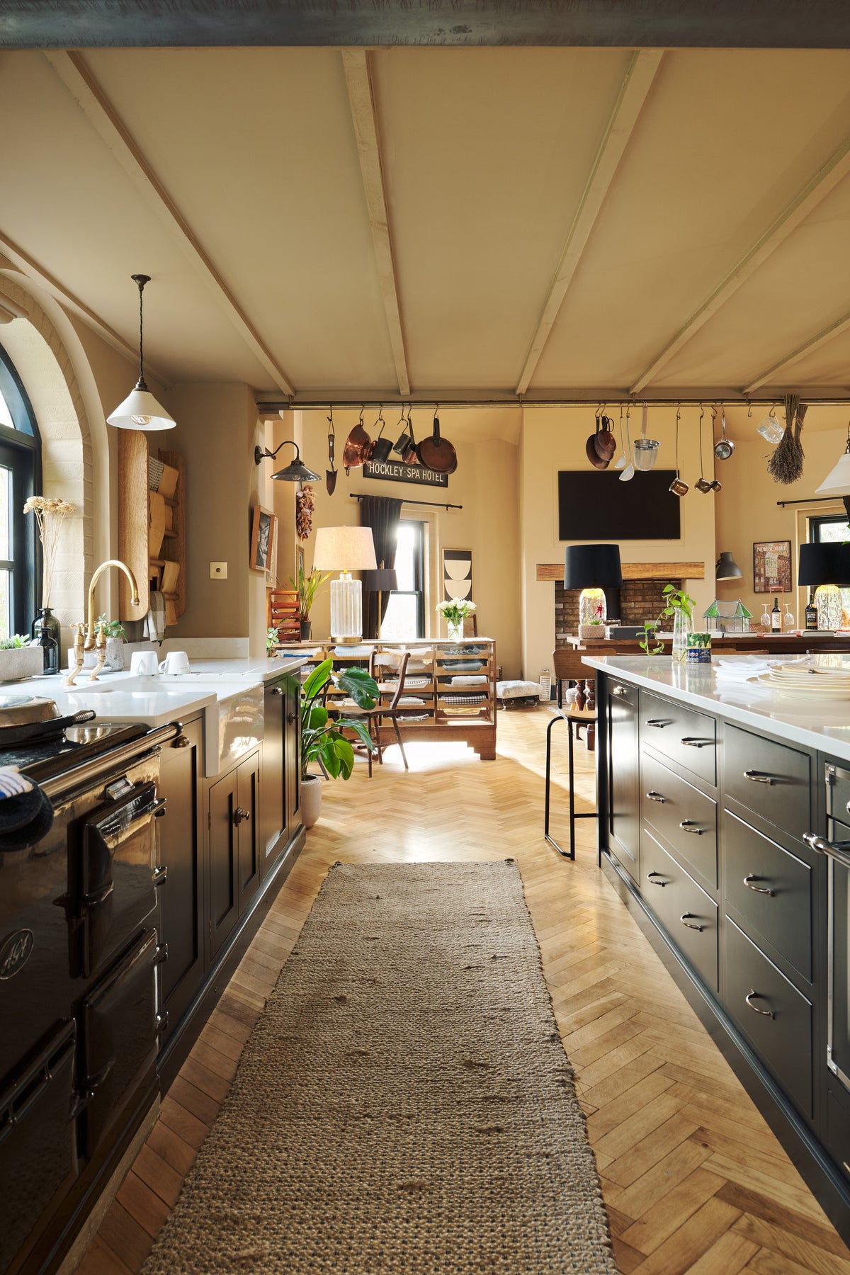 A large, open Printer’s Black Shaker kitchen. A long cooker and sink run is topped with a Silestone worktop, complemented by both an open and closed pantry larder, and a kitchen island. Decorated with a show-stopping heirloom gaselier light and an aged brass pot filler, the room feels carefully considered, comfortable and highly functional.