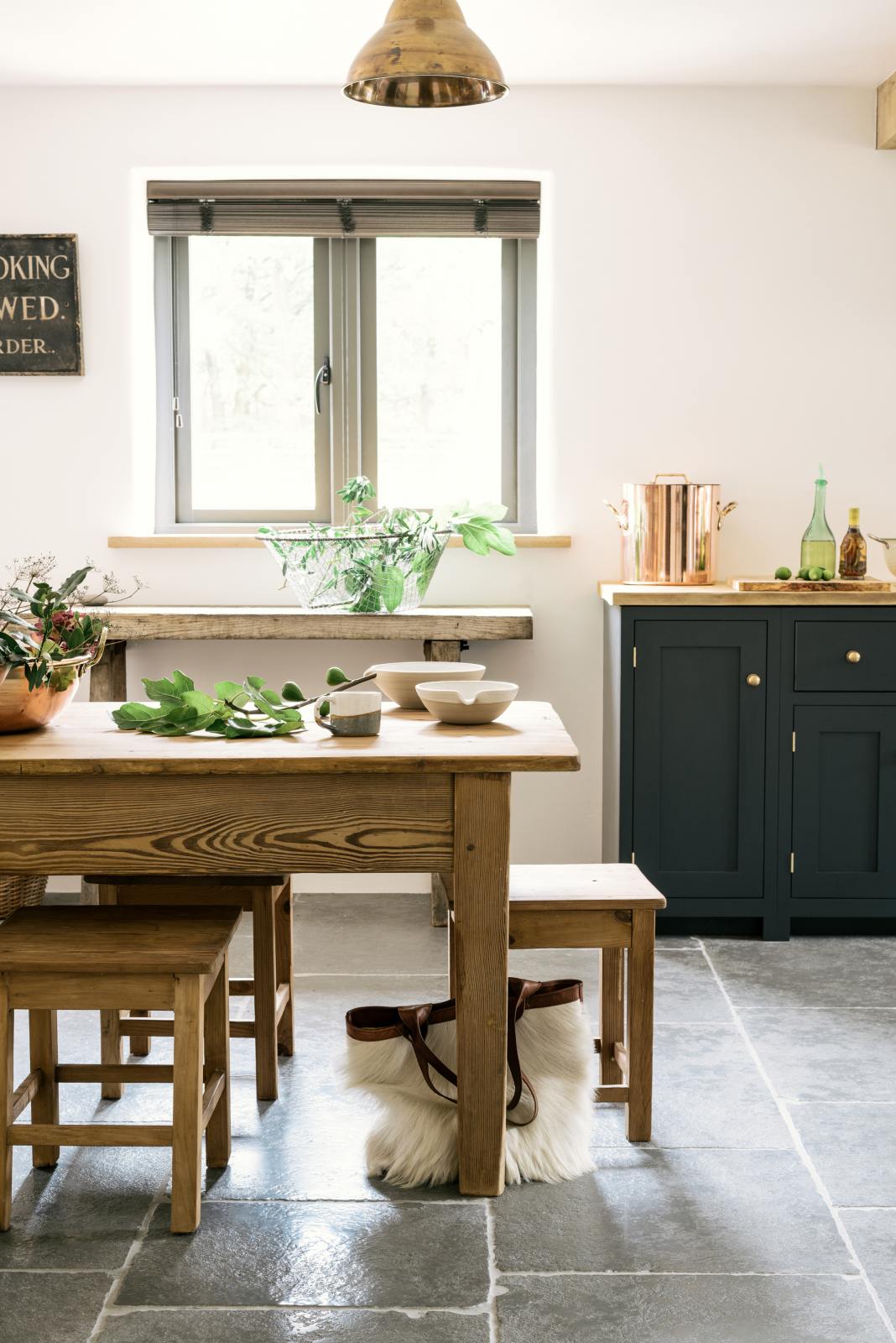A closer look at the wooden, vintage dining table with stools and the edge of the charming cottage shaker kitchen in Pantry Blue, featuring an oak worktop, steel electric cooker, splashback, canopy, and rustic stone floors.