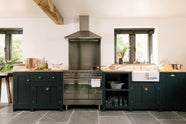 A charming cottage shaker kitchen in Pantry Blue, featuring an oak worktop, steel electric cooker, splashback, canopy, and rustic stone floors.