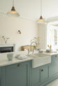 A close, angled view of the double Belfast sink in the Trinity Blue kitchen island with a Carrara marble worktop. Natural light from the original French doors brightens the simple kitchen.