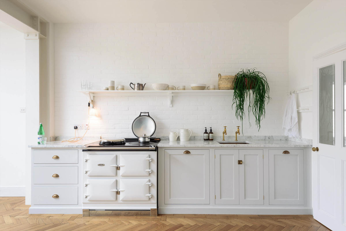 A beautiful Trinity Blue Shaker kitchen with a cooker and sink run, a long Shaker shelf overhead, a white scalloped porcelain chandelier, and grand solid oak herringbone floors.
