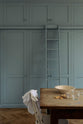 A close-up of a beautiful Trinity Blue Shaker kitchen featuring floor-to-ceiling pantry cabinets with a matching ladder, and a vintage wooden dining table with a wonderfully worn top. The table has a collection of baking equipment and ingredients.