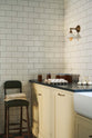 A vignette from the corner of a traditional-style scullery, with pale yellow painted Shaker base cabinets fitted with deVOL’s aged brass knobs and handles. Jars of jam, trays of eggs and fresh garlic bulbs are placed on top of the honed black granite worktop, and an antique green leather barstool is propped up.