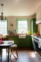 A bright and humble lime-green kitchen with an L-shaped cooker and sink run topped with aged copper worktops, a countertop and glazed cupboards, a single fluted Belfast sink with an aged brass Ionian tap, and colourful accents like tulips, a bowl of limes, macaroons, and a golden pineapple chandelier.