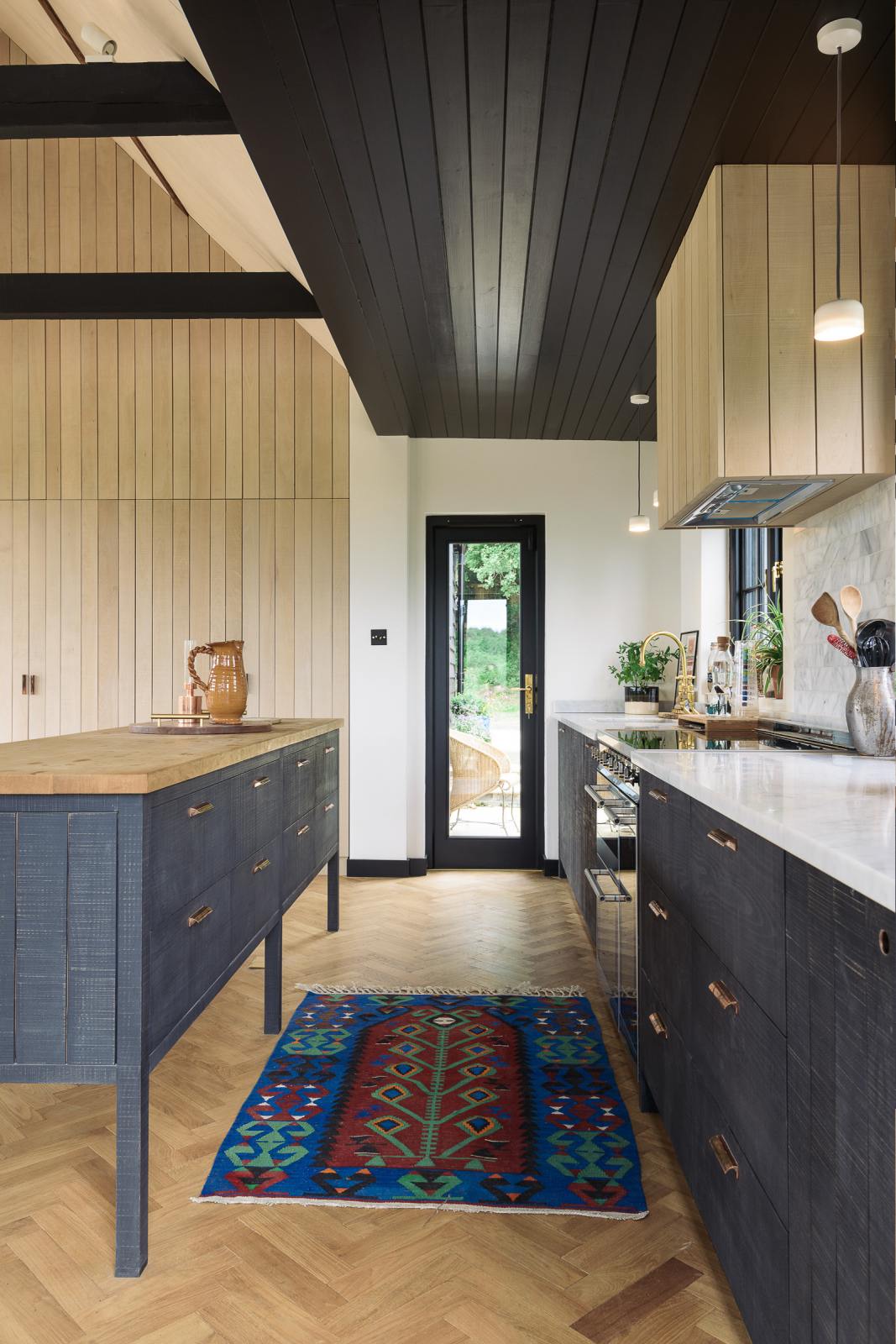 Nestled between a large and minimal Sebastian Cox kitchen, which features a long sink and cooker run with a Carrara marble worktop and a large kitchen island with a solid oak worktop, is a built-in bank of cupboards and a slim glass door leading to the gorgeous countryside of Tuscany. Beautifully decorated with artisan ceramics and a bright patterned rug, this kitchen creates a simple and practical space.