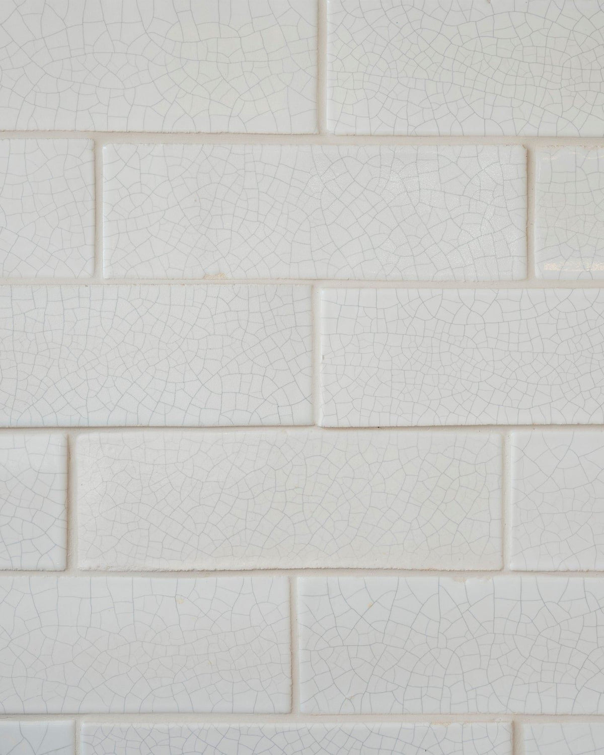 A close-up view of glossy white metro wall tiles with delicate charcoal crazing across the surface. TEST