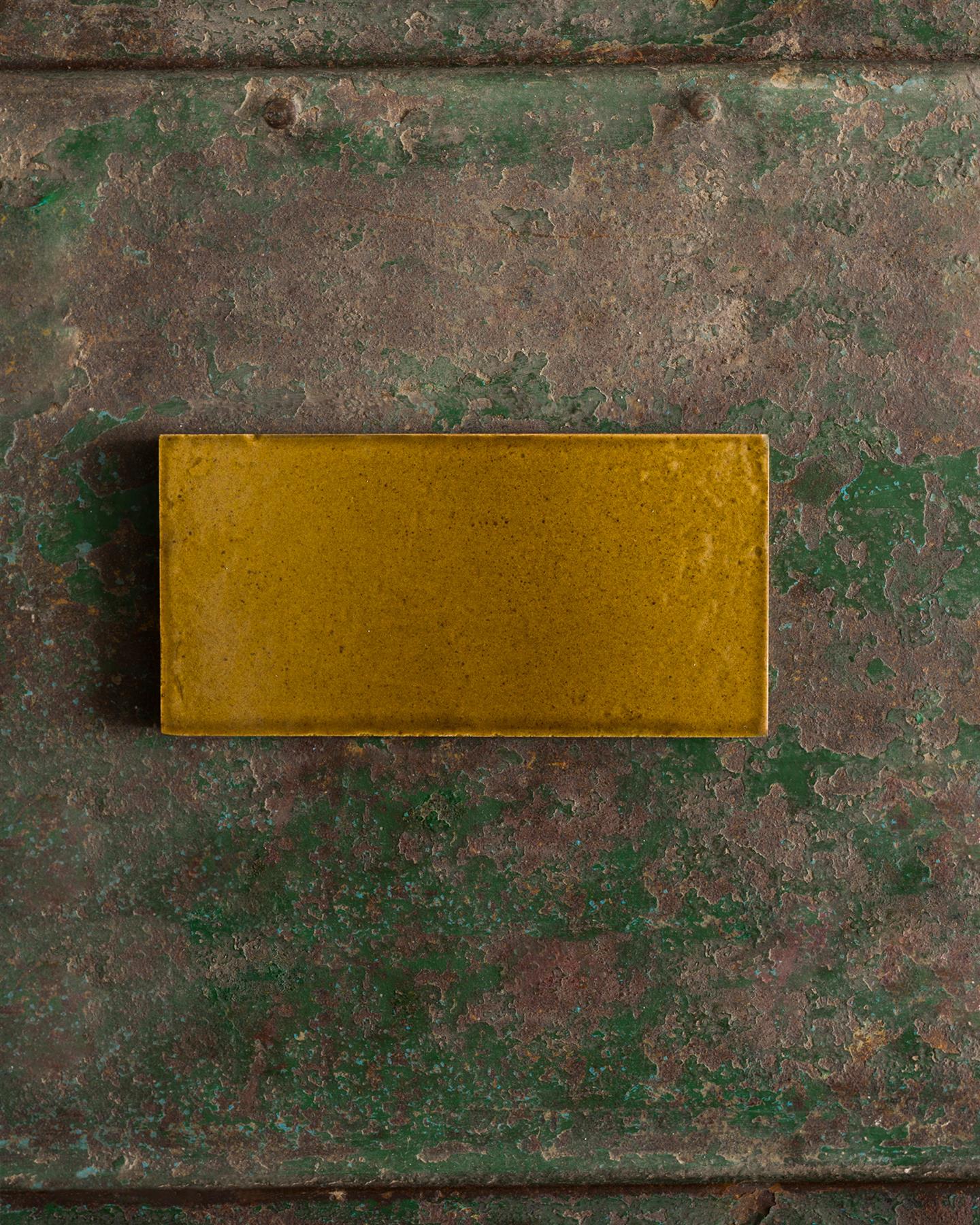 A glossy sepia metro tile on a rustic metallic surface.
