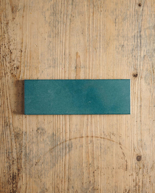 A glossy teal wide metro tile on a rustic wooden surface. | Plain Long Metro