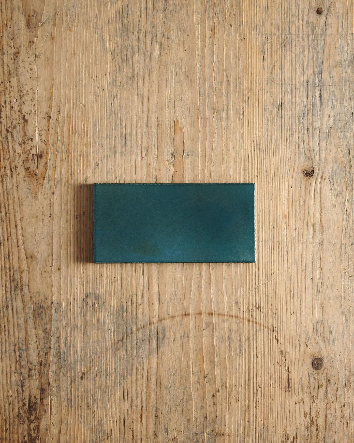 A glossy teal metro tile on a rustic wooden surface.
