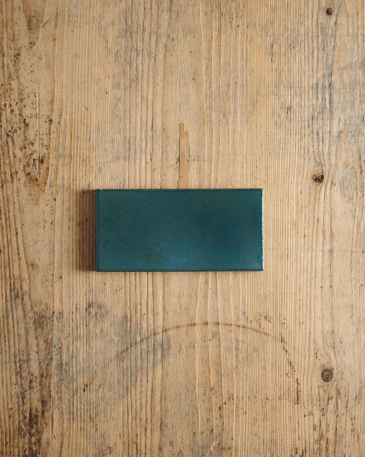 A glossy teal metro tile on a rustic wooden surface. | Plain Metro