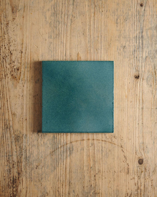 A glossy teal square tile on a rustic wooden surface. | Plain Square