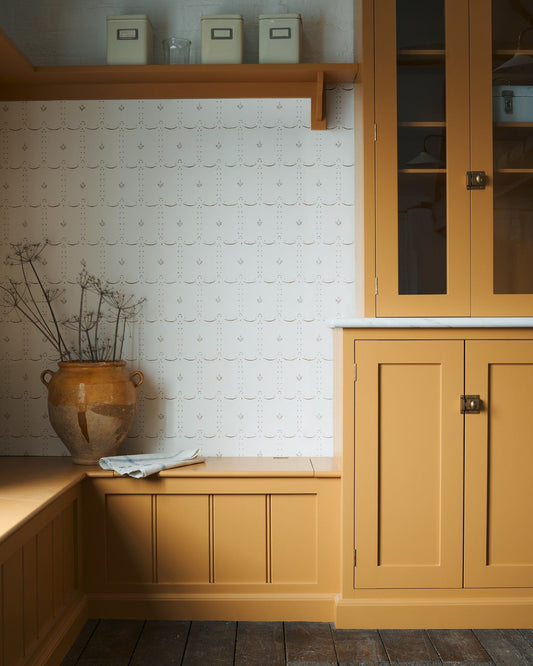 An off-white wallpaper with a delicate hand-painted pattern in a sepia colour, next to Shaker-style cupboards in mustard yellow colour.|Petite Ditsy Delft in Sepia